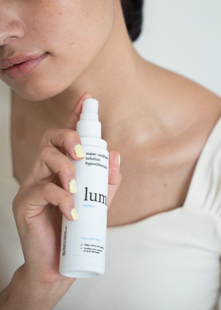 Hand holding Lumi Derma spray bottle